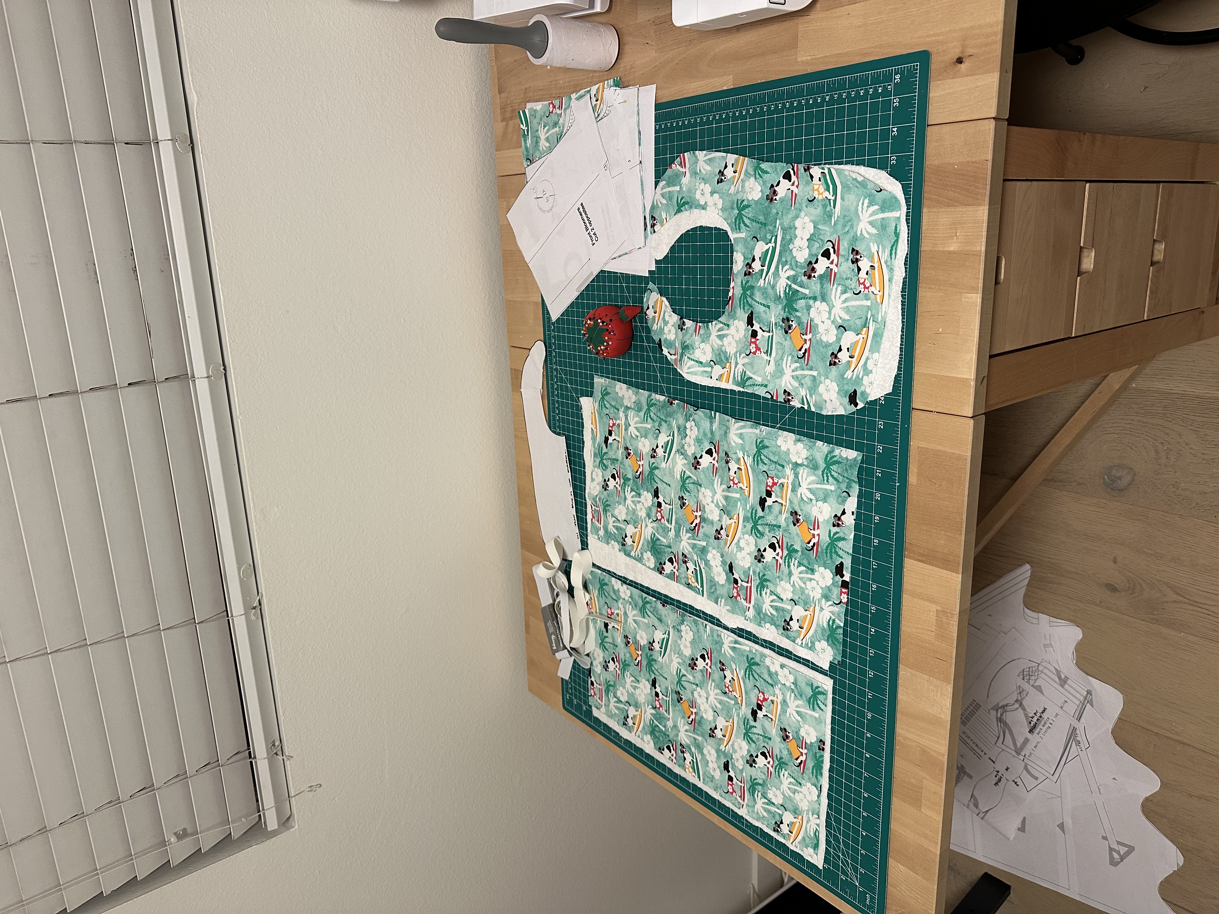 Behind the scenes: bib and burp cloth pieces cut out in teal surfing dogs fabric on a cutting mat