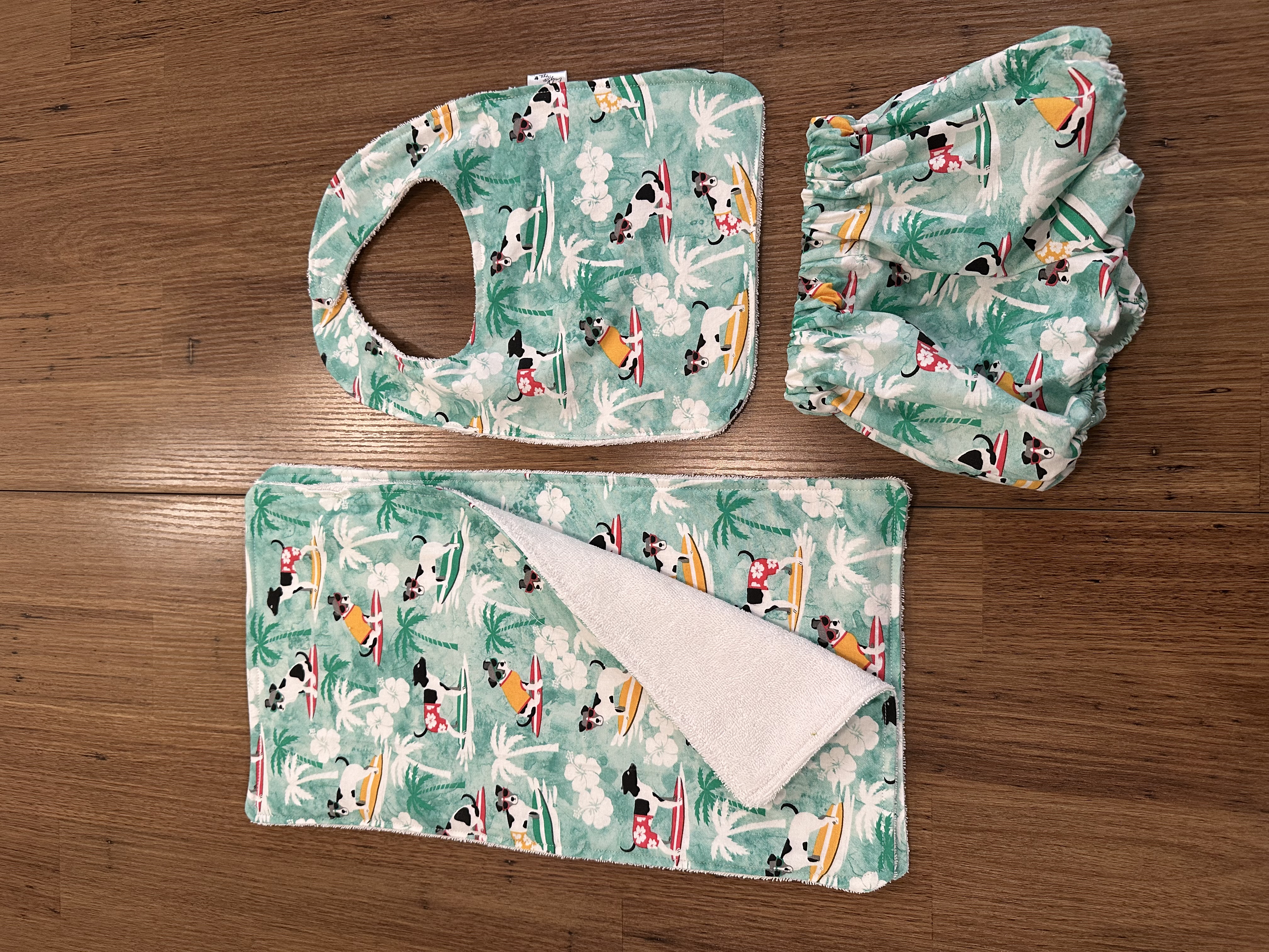 A matching bib, burp cloth, and bloomers set in a teal surfing dogs print