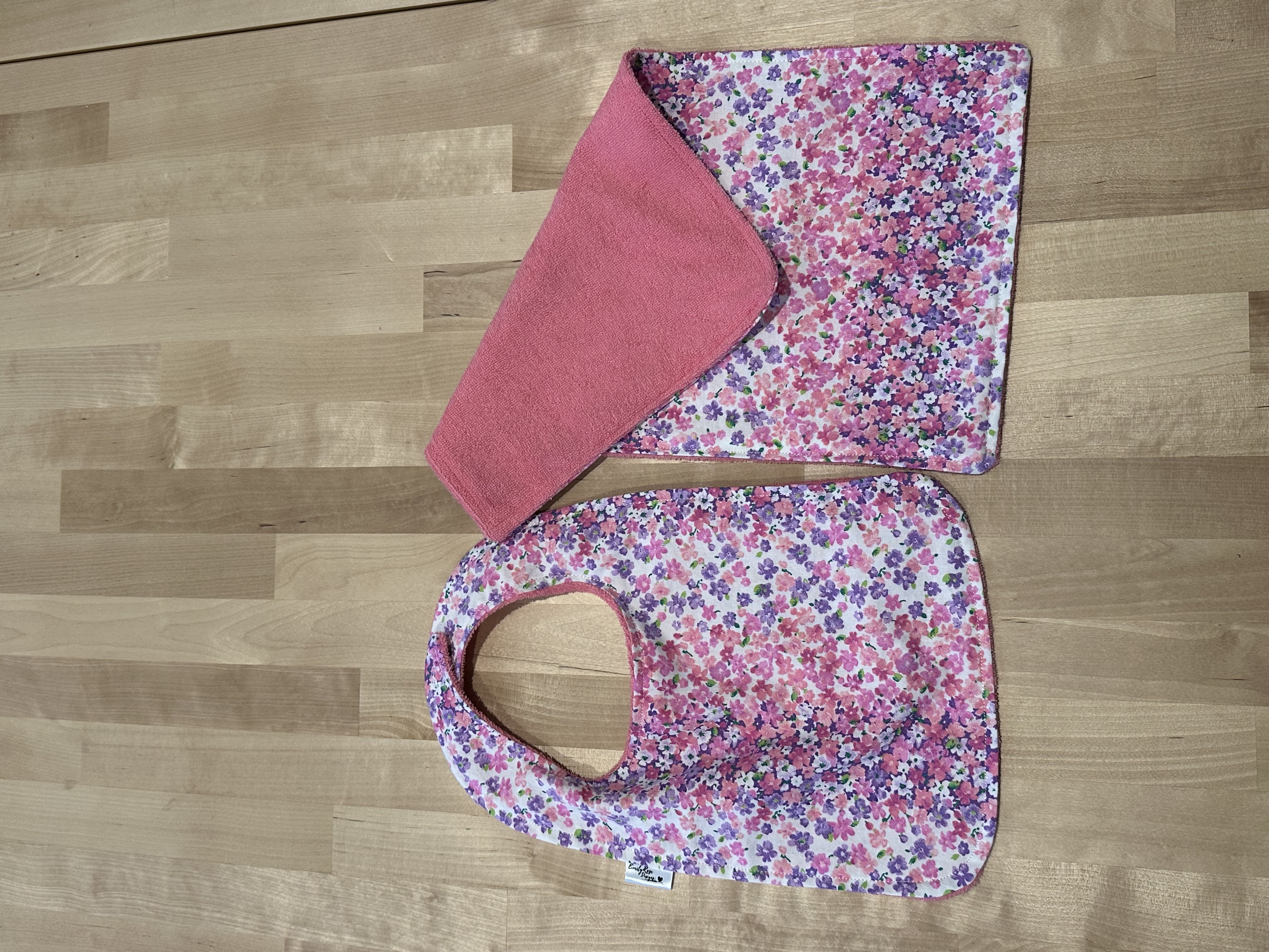 A finished bib and burp cloth set in a pink floral print with pink terry on the reverse