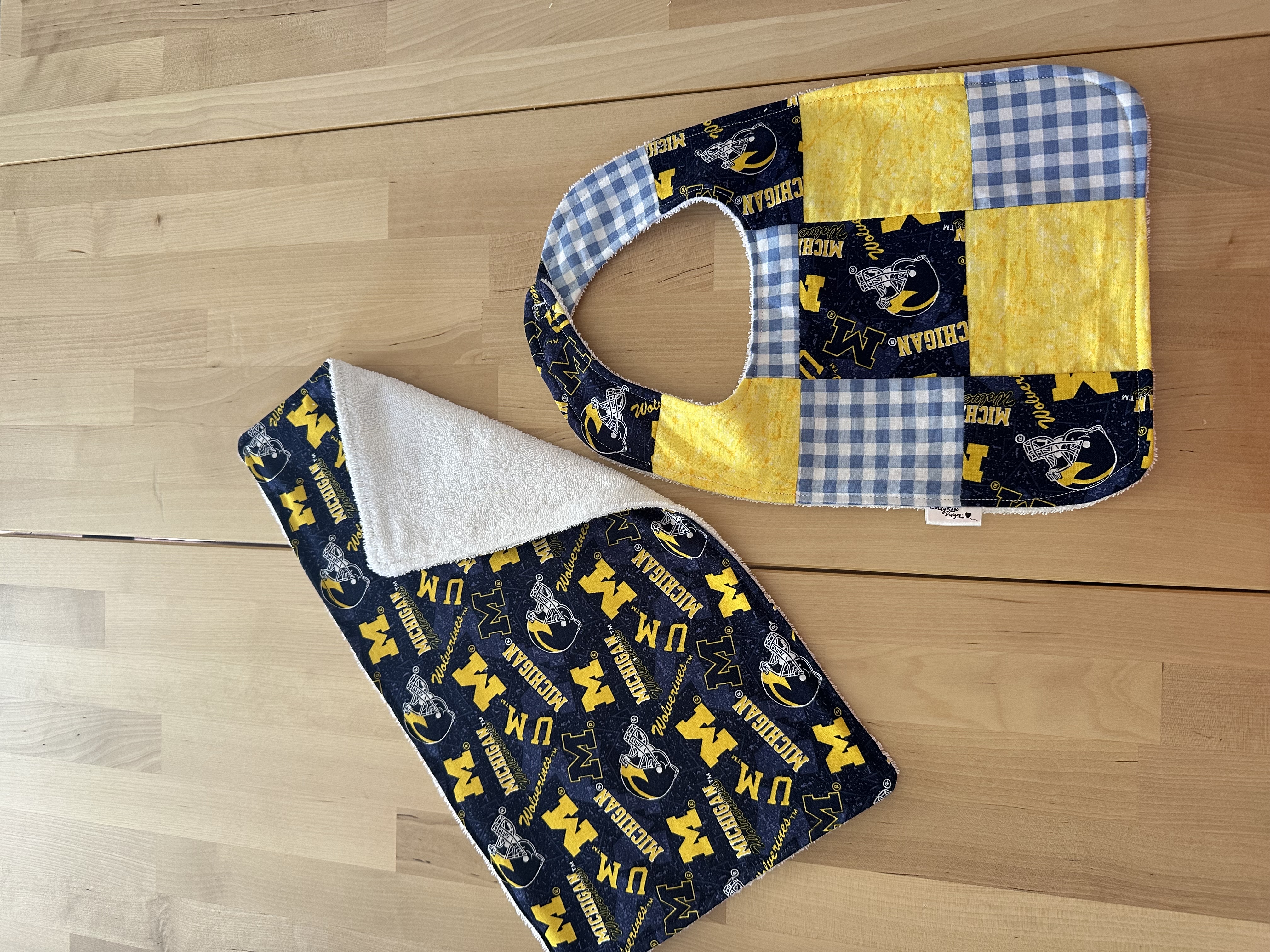 A quilted University of Michigan bib in patchwork blocks with a matching Michigan print burp cloth