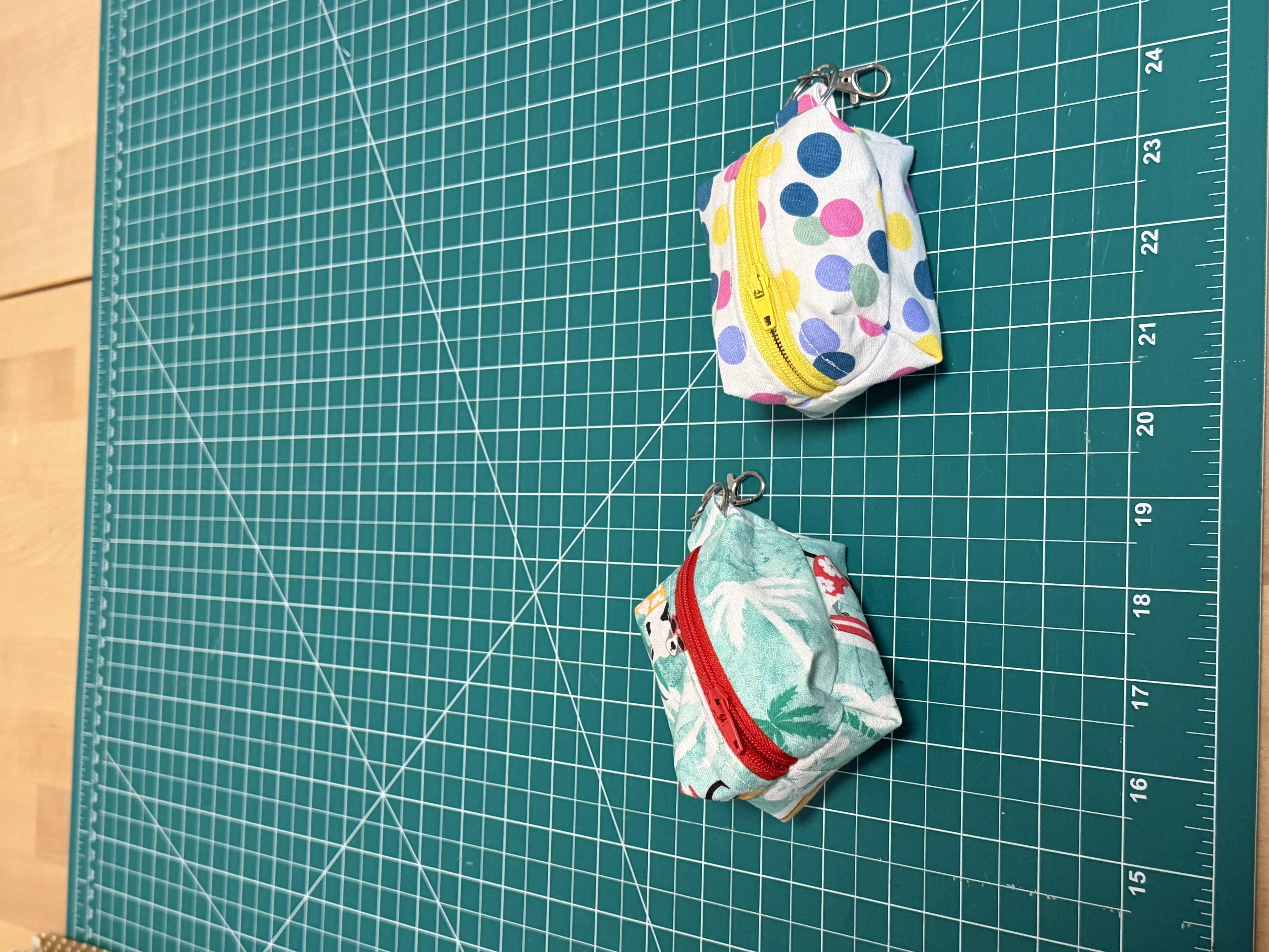 Two finished dog poop bag holders hanging by their clips, one in a tropical dog print with a red zipper and one in a polka dot print with a yellow zipper